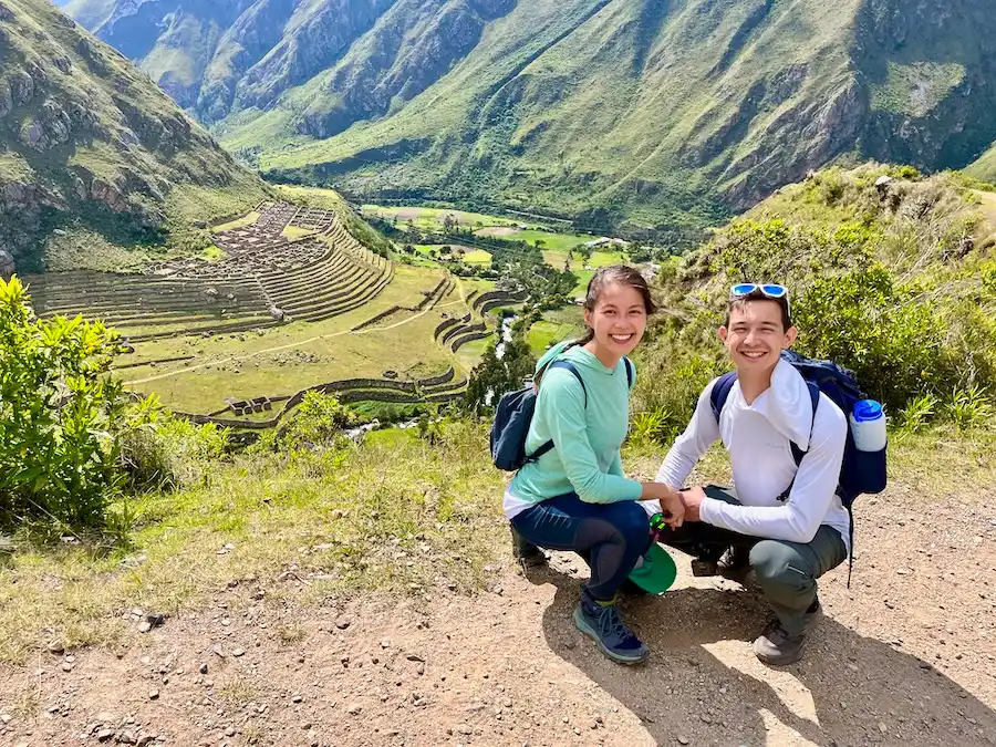 Two hikers crouched down to take a photo of an Inca site in the background.