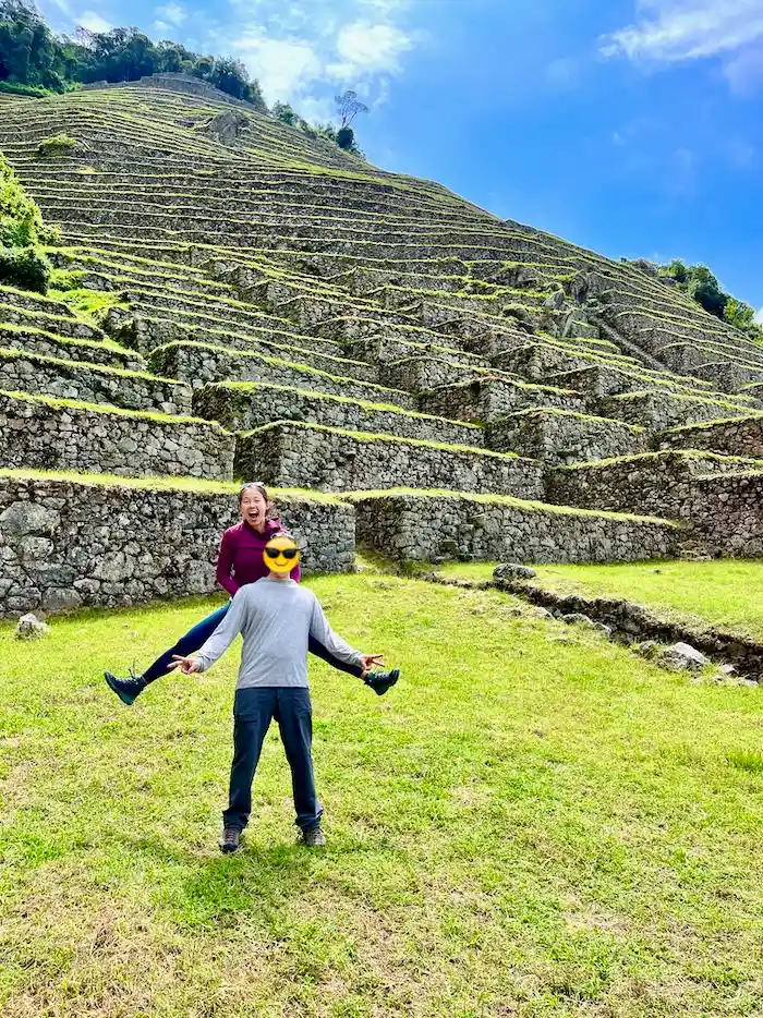 Two people standing in front of a stairs of ruins that run very high with grass growing on top.