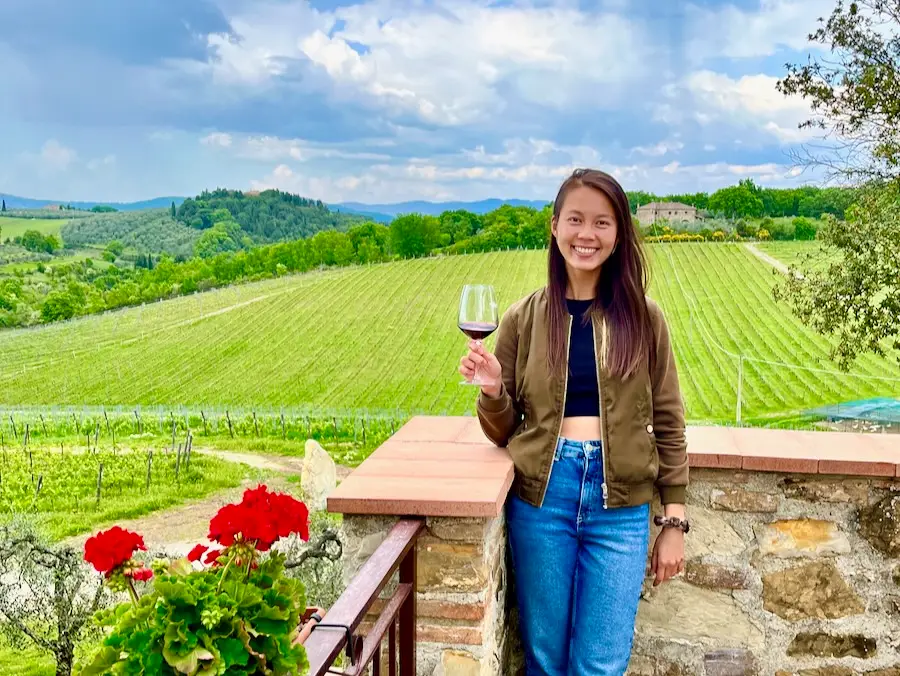 A woman holding a glass of red wine against a field of grapes.