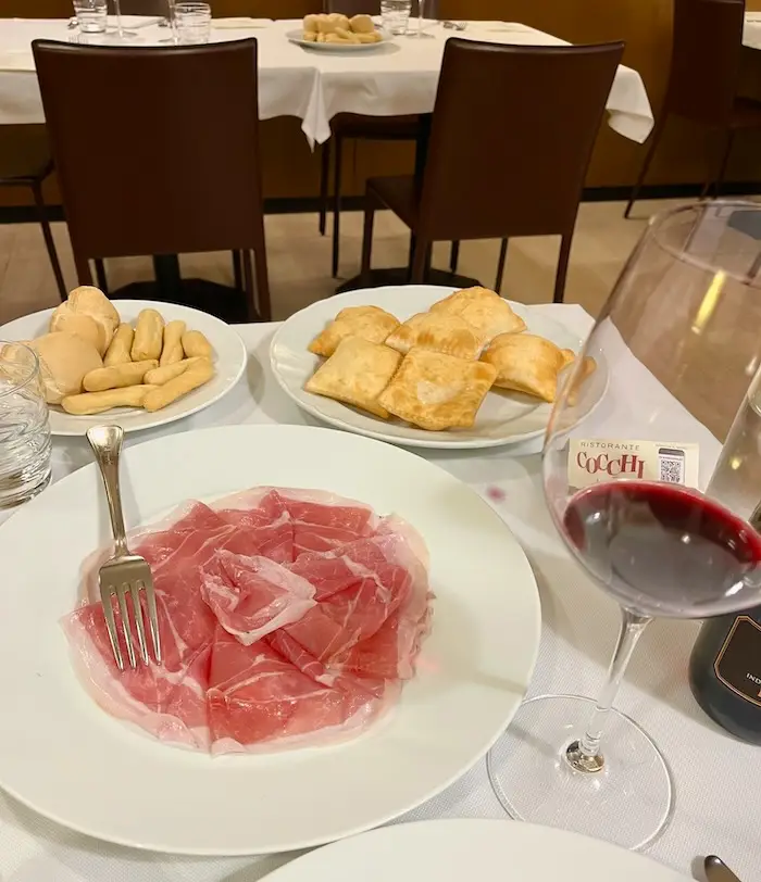 A plate full of cured meat with a glass of red wine.