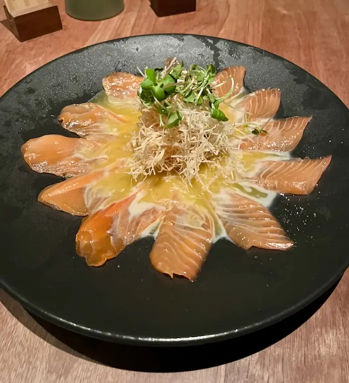 A black plate holding cured salmon dipped in a citrus sauce.