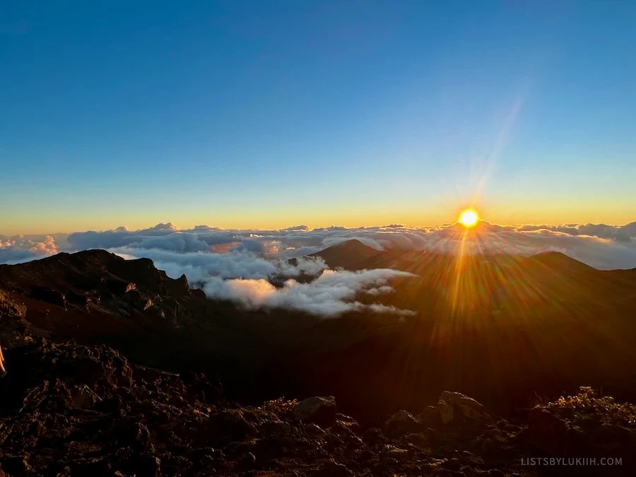 A sun's rays peaking through the clouds over mountains.