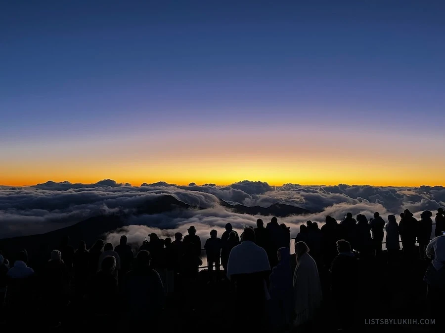 Many people lined up on the side of a mountain waiting for the sun to rise.