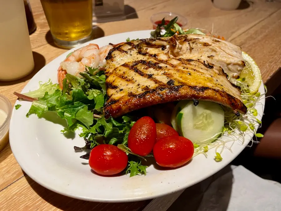 A plate with a grilled fish fillet and some salad underneath.
