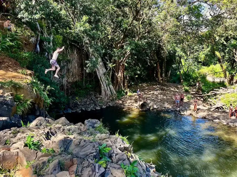 A man jumping off a cliff into a swimming hole.
