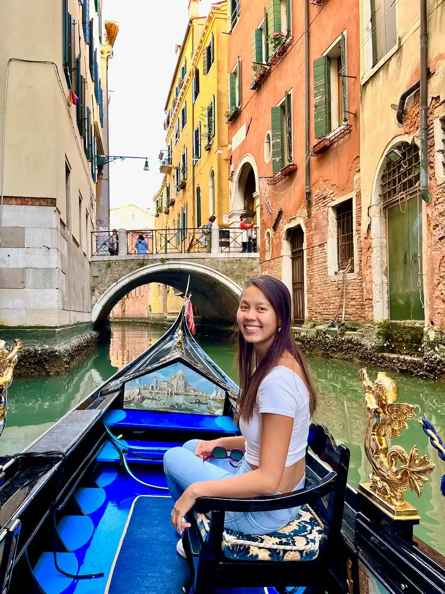 A woman sitting on a boat floating on a small canal surrounded by colorful buildings.