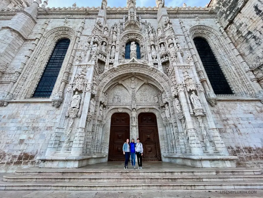 Three women standing in front of a white, ornate building entry.