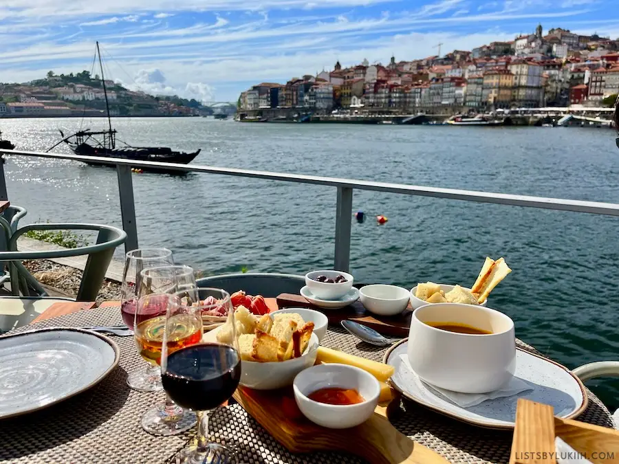 Port wine, cured ham and bread meal overlooking a water view with European buildings in the background.