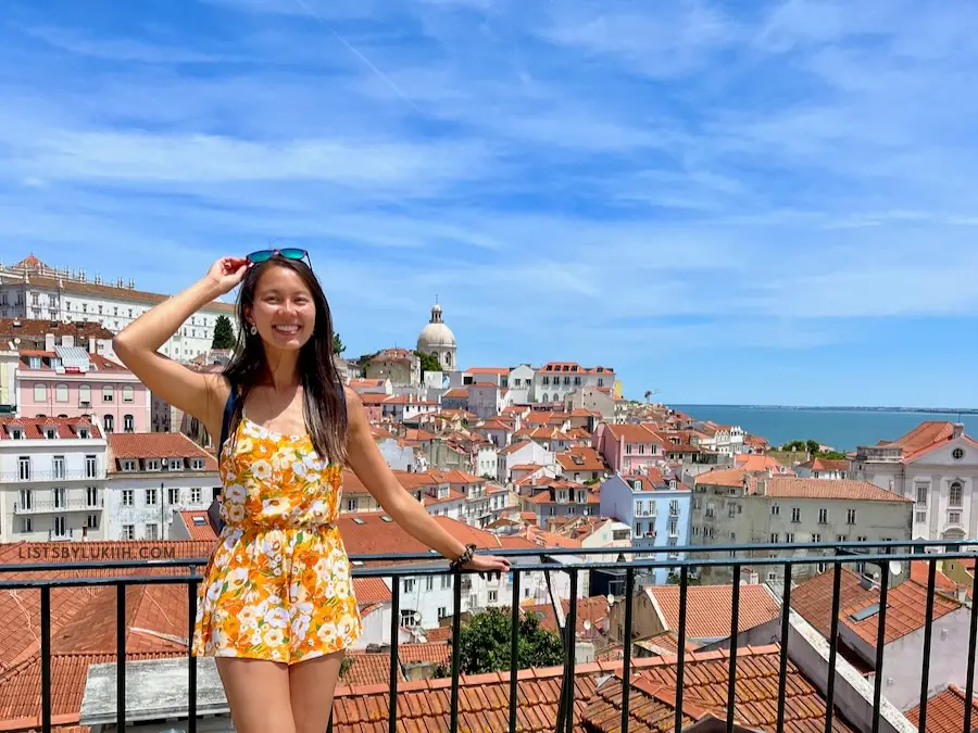 A woman on a balcony overlooking a background with buildings with orange-clay roofs.