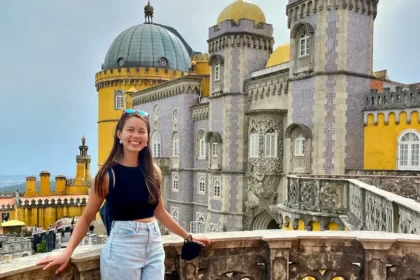A woman standing in front of a historic yellow and purple castle.