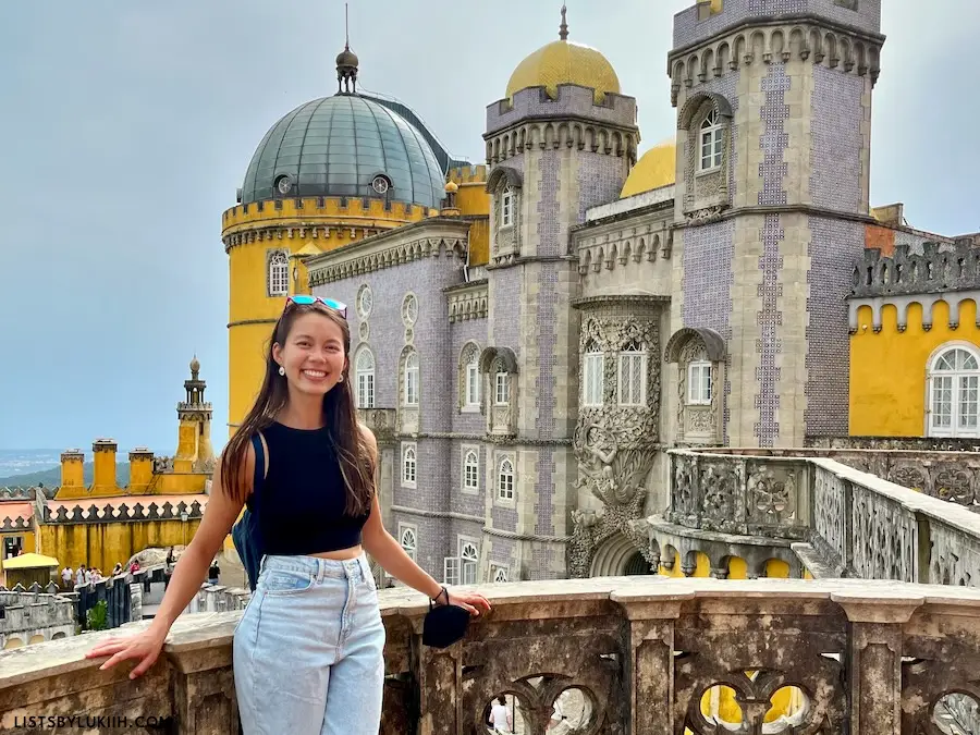 A woman standing in front of a historic yellow and purple castle.