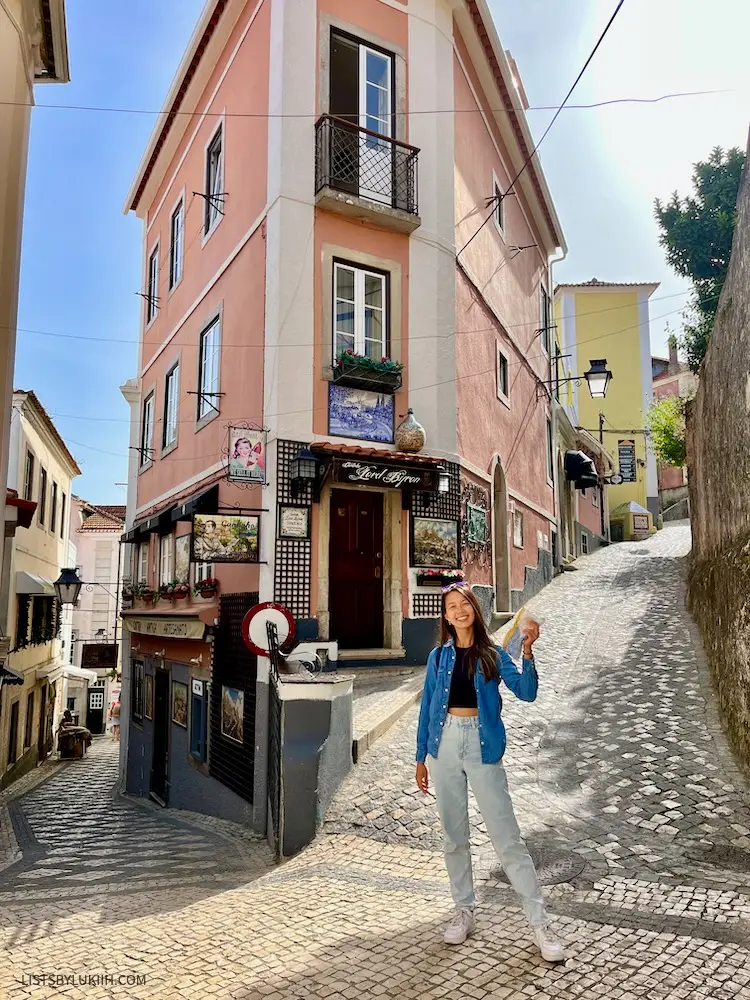 A woman standing on a narrow, cobble stone alley way with an orange building in the background.