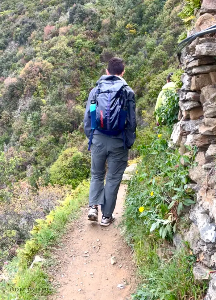A person walking on a narrow trail next to the side of a mountain.