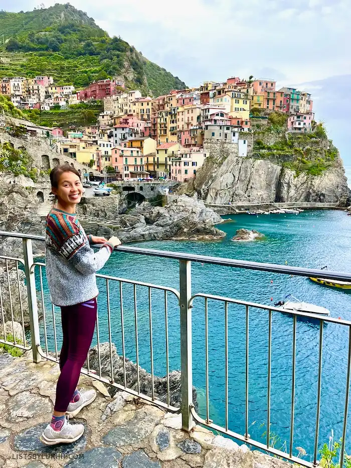 A woman standing in front of a background with colorful buildings on a mountain by the ocean.