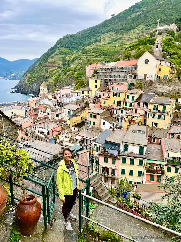A woman standing on a balcony overlooking colorful buildings by a mountain.