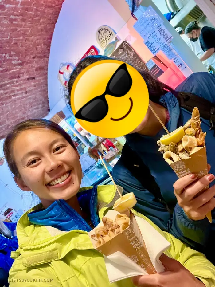 Two people holding a cone with fried seafood in them.