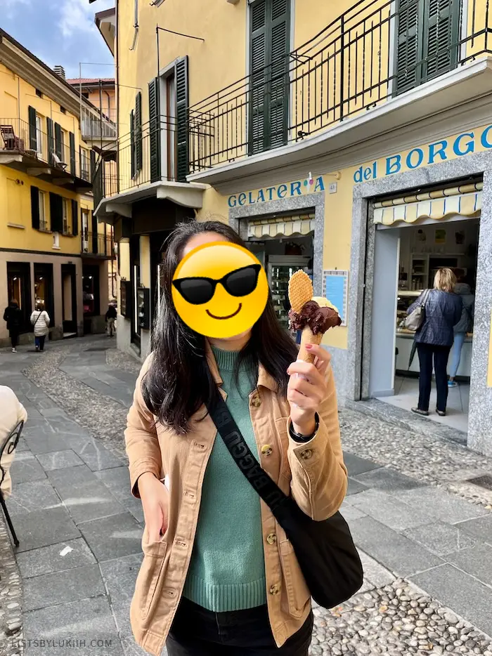 A woman holding a gelato while standing in a narrow, pedestrian-friendly street.