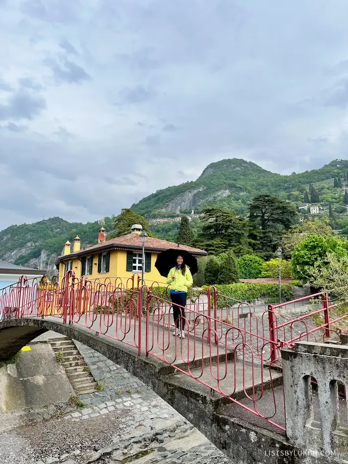 A woman standing on a red bridge with a lush, green mountain behind her.