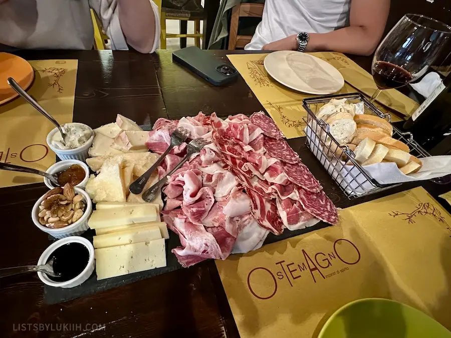 A board covered with cured meat, bread, cheese and jam.