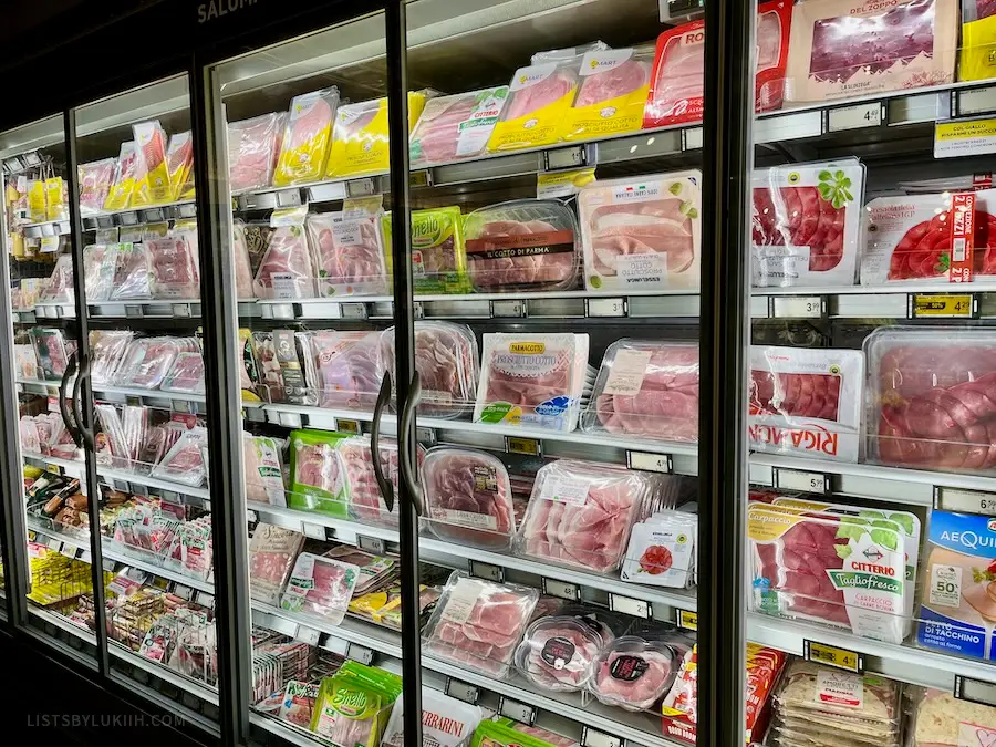 A grocery store fridge filled with different selections of cured ham.