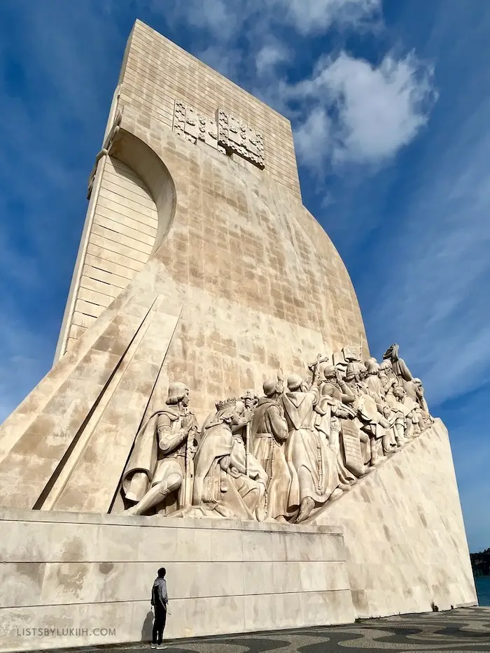 A person standing next to a big, white structure with several people carved into it.