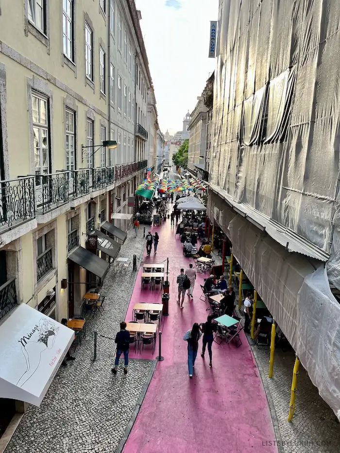 A pedestrian-friendly street painted in Pink and covered in colorful umbrellas in one portion.