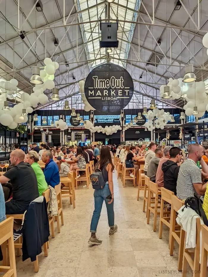 A woman walking through a food court with the sign that says Time Out Market Lisboa.