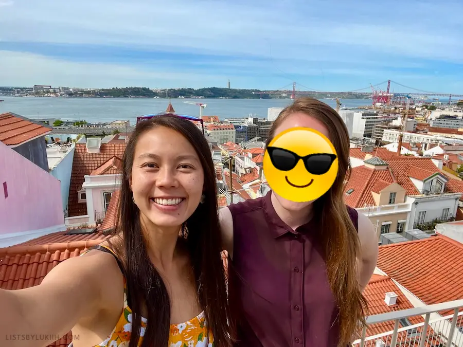 Two women taking a selfie on a balcony, with orange rooftops in the background.