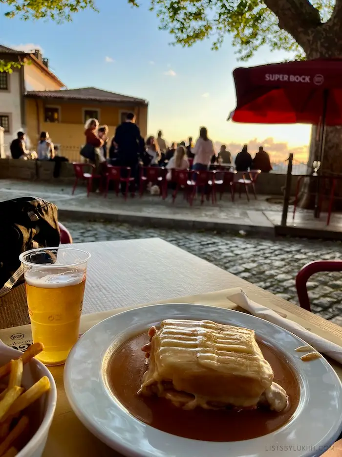 A beer and sandwiched covered in sauce on an outdoor table.