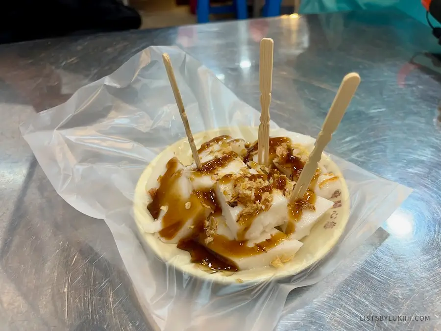 A bowl holding white, soft, edible cubes covered in shallots and thick soy sauce.