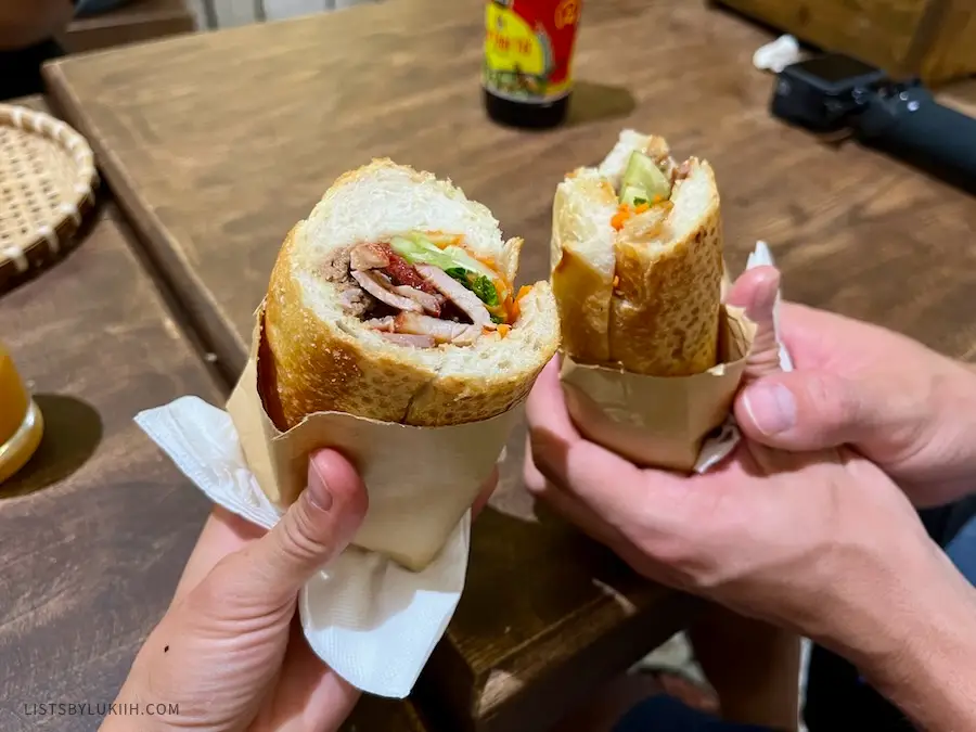 Two baguette sandwiches with pork belly and vegetables.