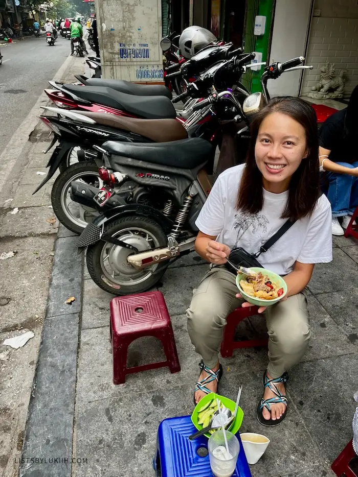 A woman sitting on the street next to parked motorbikes.