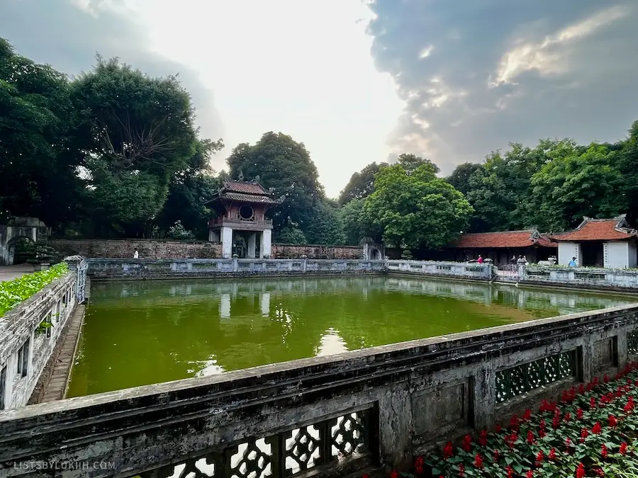 A big pool of green water inside a large complex surrounded by an Asian gate and trees.