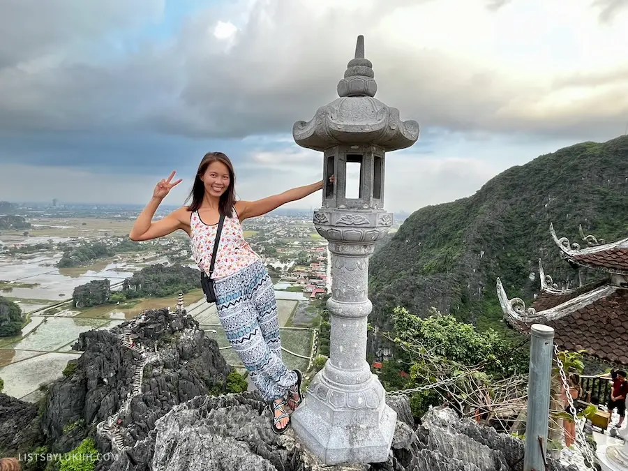 A woman standing on a steep mountain stone overlooking a watery field view.