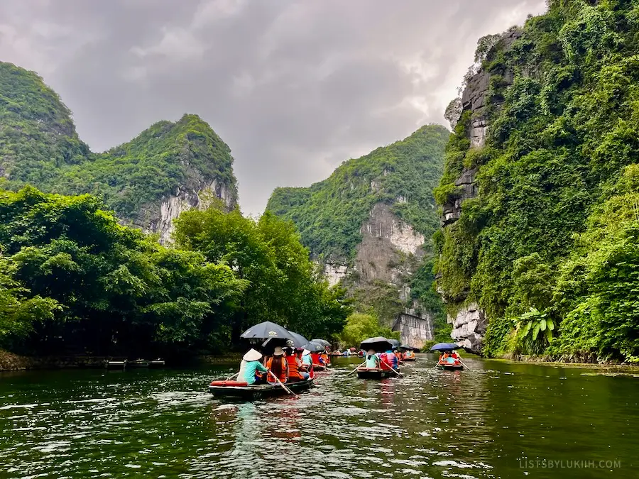 Multiple wooden boats on an emerald water river through limestone mountains.