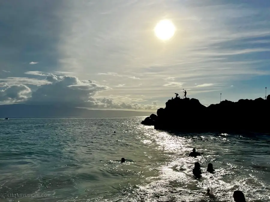 People at the top of a rock ready to jump into the ocean.