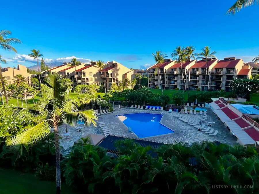 A view of a condo community with a pool in the middle surrounded by palm trees.