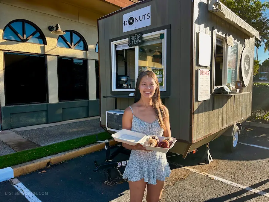 A woman holding a plate of donuts by a food truck.