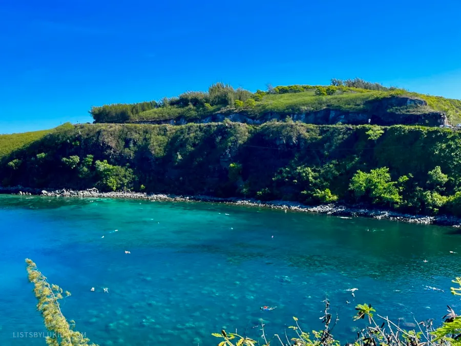 A view of a blue ocean water with a sailboat and people snorkeling.