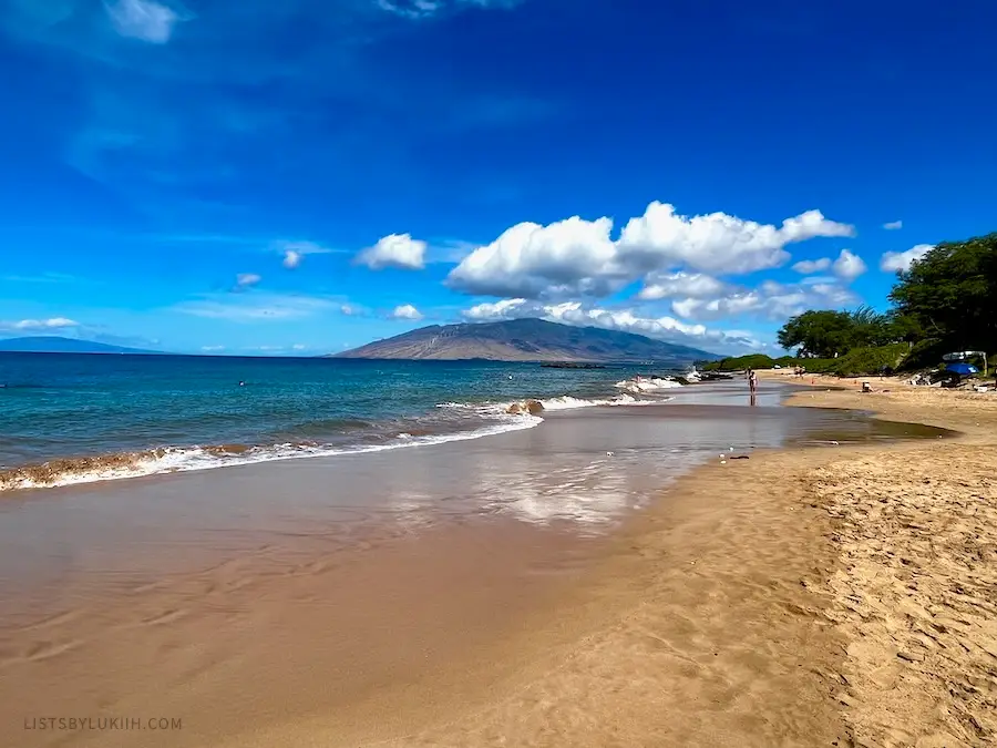 A wide beach with blue ocean and a mountain in the background.