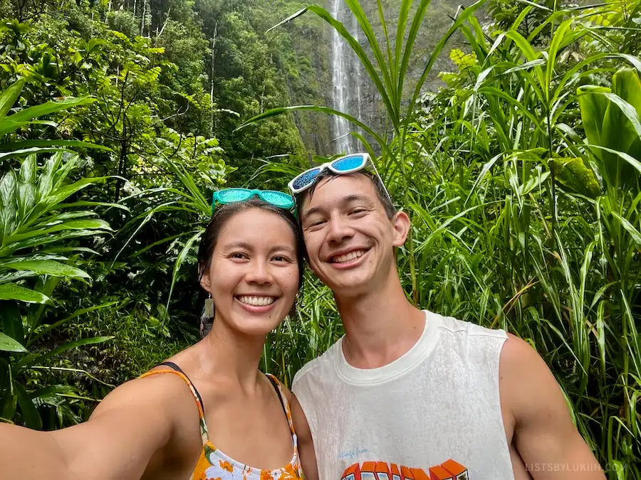 Two people wearing sunglasses in a jungle in front of a waterfall.