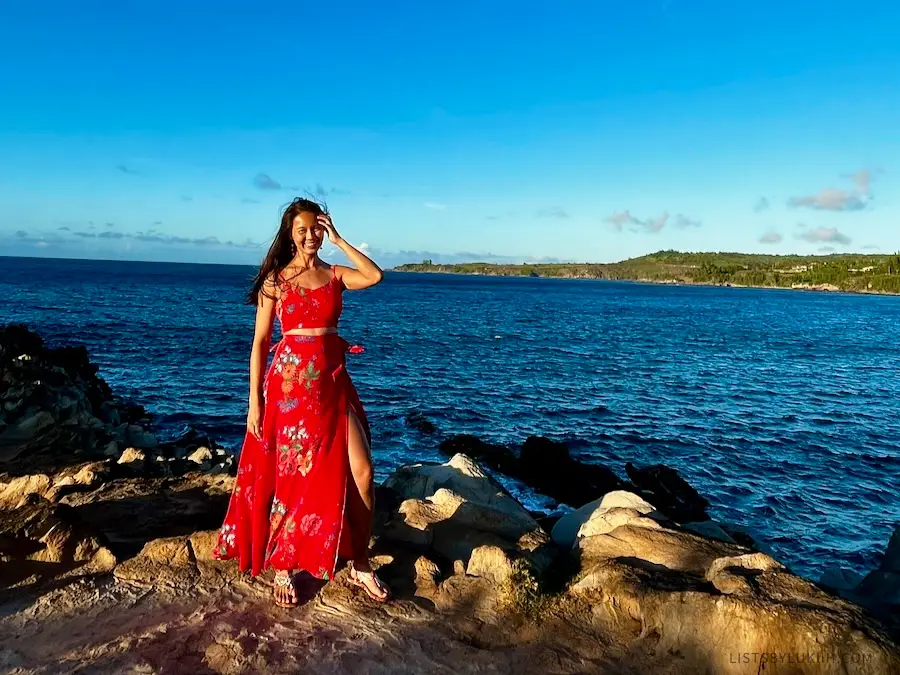 A woman wearing a dress and sandals at the edge near the ocean.