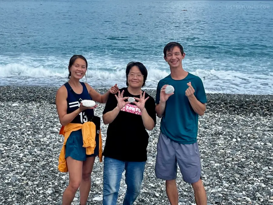 Three people holding a white rock in front of a blue ocean.