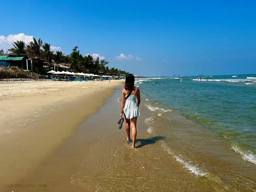 A woman walking on a beach with blue water.