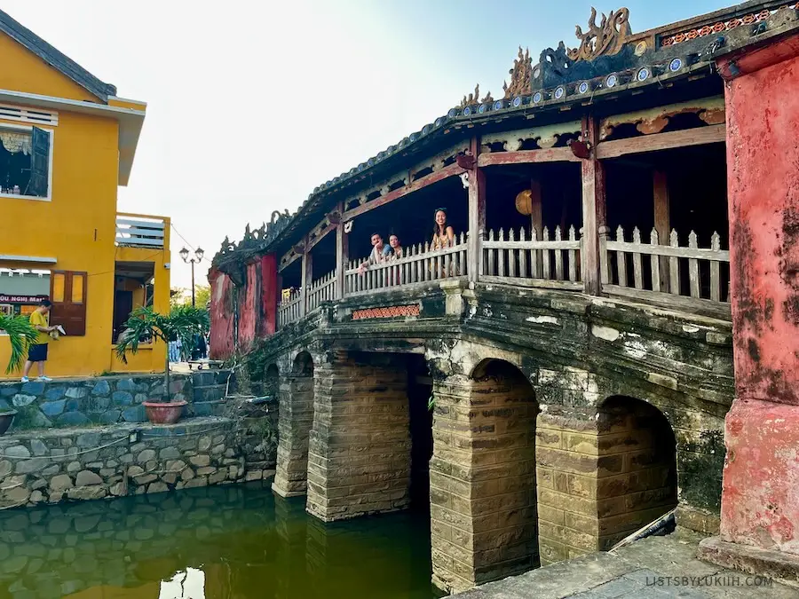 A woman standing inside a small and ancient bridge with a dragon decoration at the top.