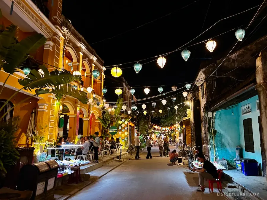 A street decorated with brightly-lit lanterns at night while people have dinner at restaurants.