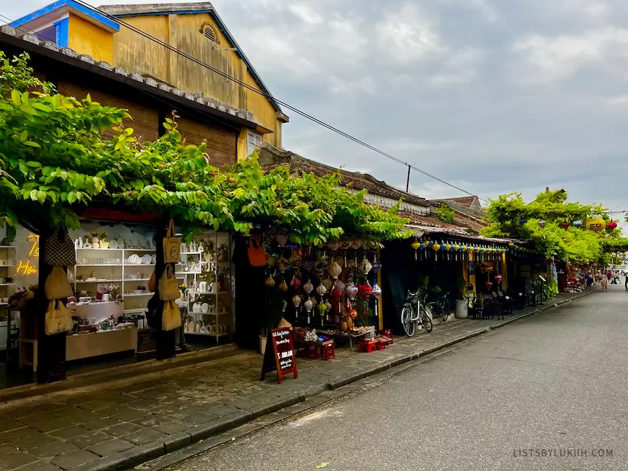 A street with open-air shops selling lanterns and bags.