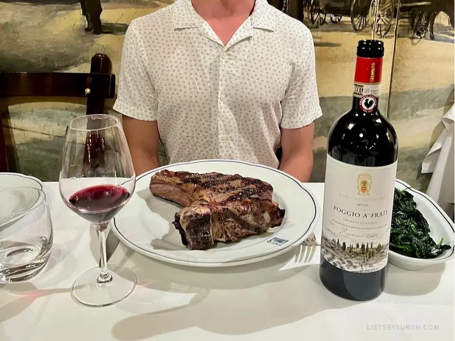 A thick-cut t-bone steak on a plate next to a cup and bottle of wine.