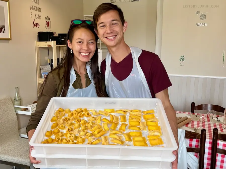 Two people holding a large container with pre-cooked pasta in it.