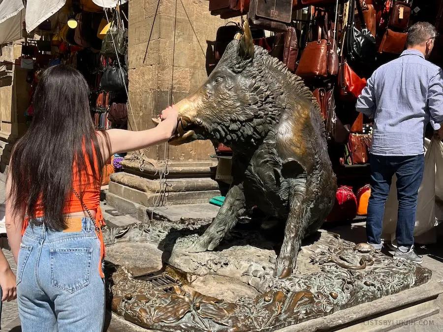 A woman touching the nose of a pig statue.